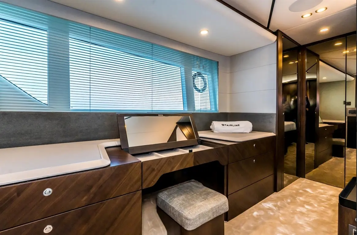 Luxurious yacht cabin featuring a desk with a mirror, wooden storage, and blue blinds, showcasing a modern design aesthetic.
